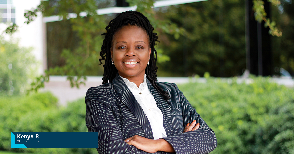 Kenya P., Capital One VP of Operations, stands outside in front of greenery and smiles with her arms crossed